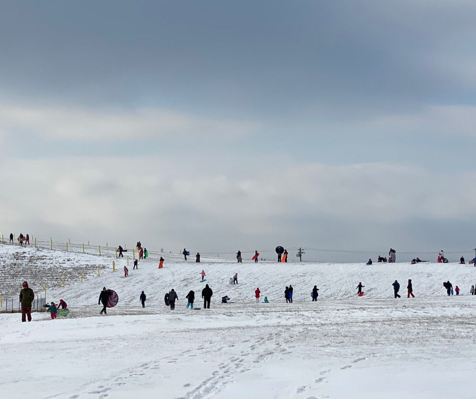 Kids and adults ridding down a hill during wintertime. 