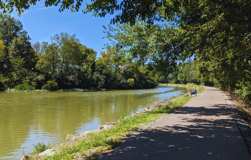 ApavedwalkingandbikingtrailintheshadenexttotheGreatMiamiRiverwithamanfishing